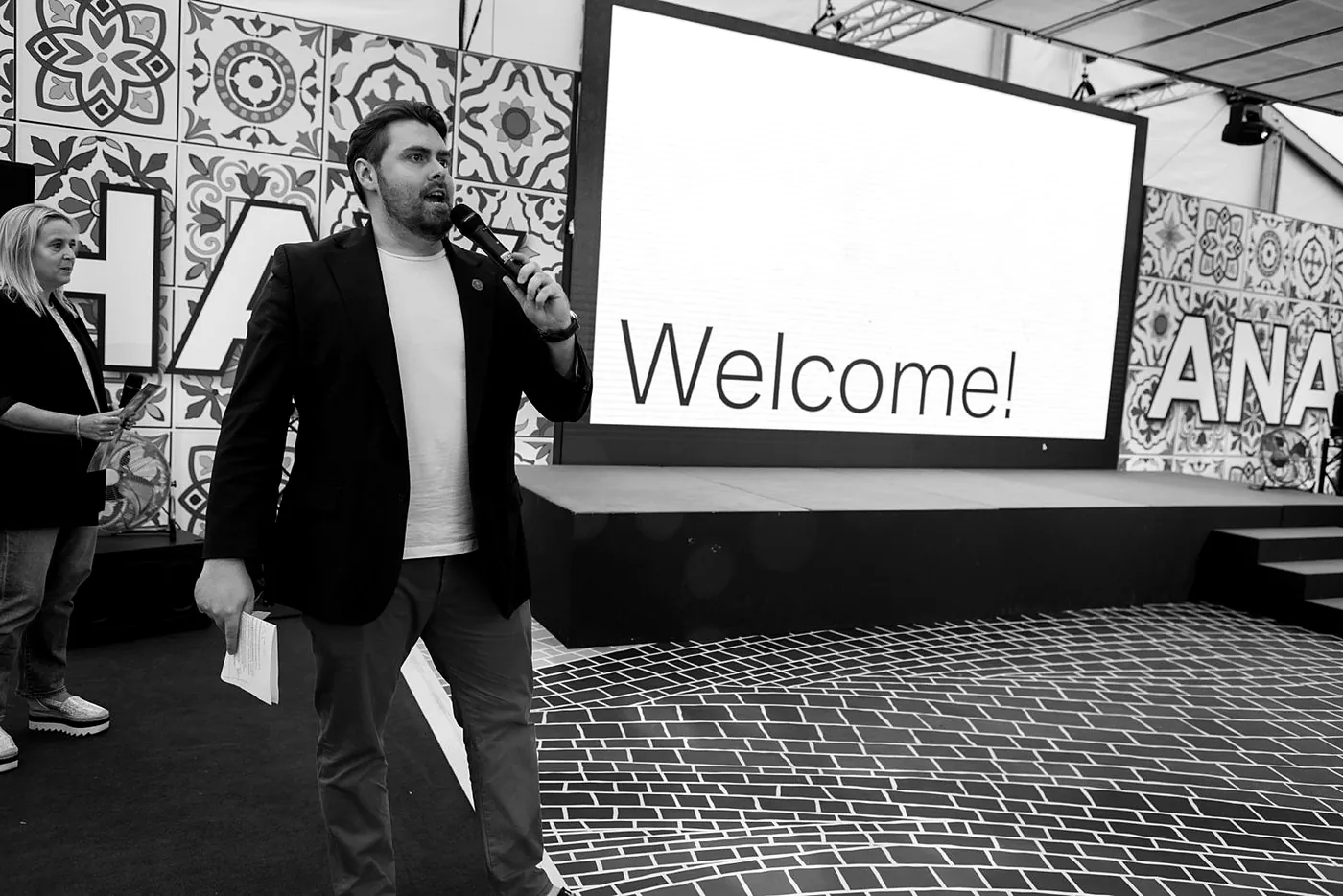 Rhys Morris, master of ceremonies, opening an event on stage in front of a Welcome screen